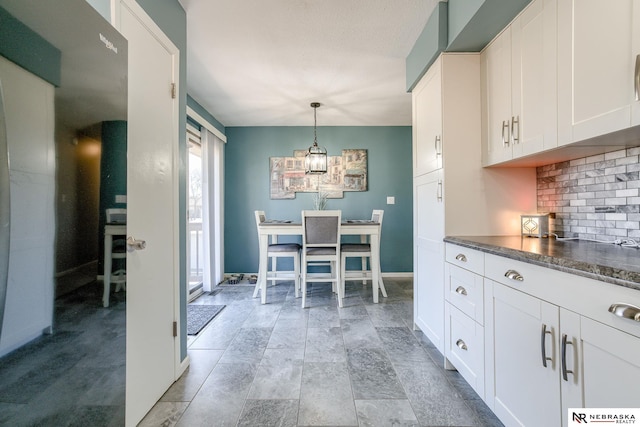 kitchen with dark countertops, tasteful backsplash, baseboards, hanging light fixtures, and white cabinets