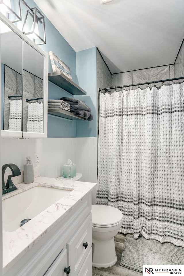 full bath with vanity, a shower with shower curtain, toilet, and a wainscoted wall