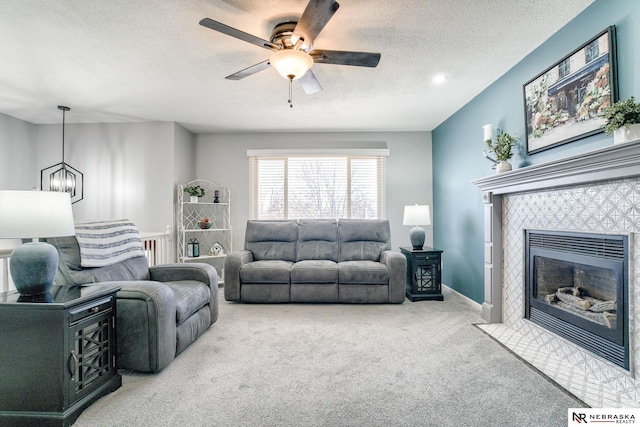 living room with ceiling fan with notable chandelier, a textured ceiling, carpet, baseboards, and a tile fireplace