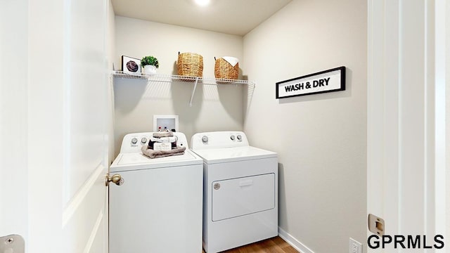 clothes washing area with washing machine and clothes dryer, laundry area, baseboards, and wood finished floors