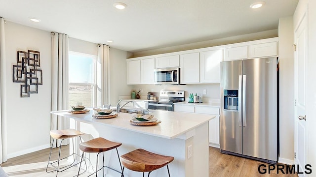 kitchen featuring a center island with sink, light wood-style flooring, a sink, stainless steel appliances, and a kitchen bar