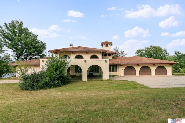 mediterranean / spanish-style house featuring a tile roof, a front yard, stucco siding, a garage, and driveway