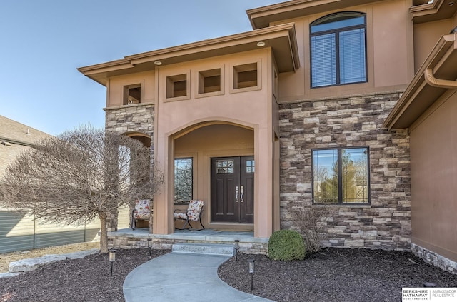 view of exterior entry with stone siding, stucco siding, and a porch