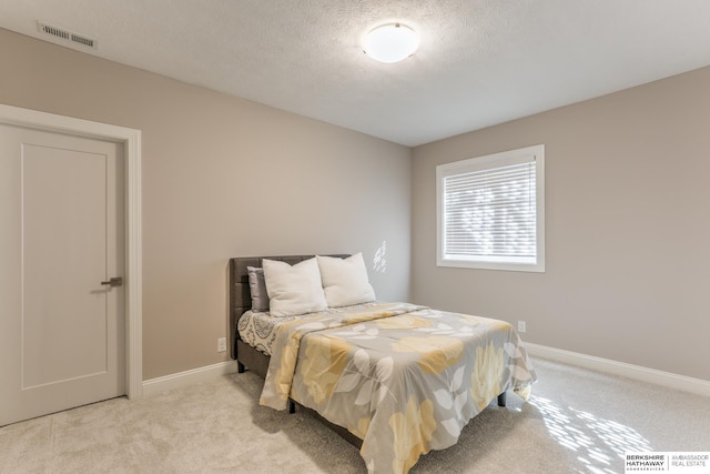 bedroom featuring a textured ceiling, baseboards, visible vents, and light carpet