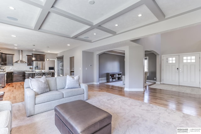 living room with arched walkways, light wood finished floors, coffered ceiling, and baseboards