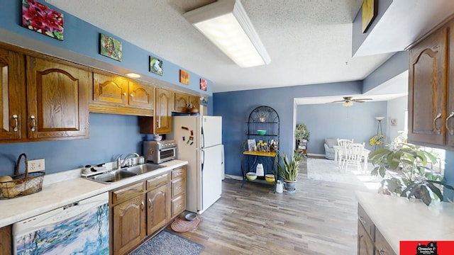 kitchen with light countertops, light wood-style flooring, white appliances, a ceiling fan, and a sink