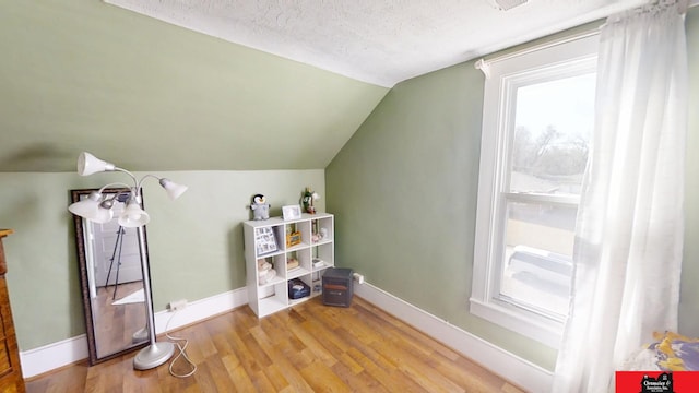 bonus room with a textured ceiling, lofted ceiling, baseboards, and wood finished floors