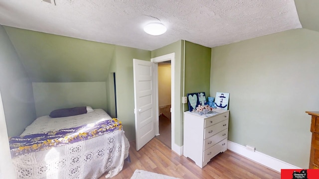 bedroom featuring light wood-type flooring, lofted ceiling, a textured ceiling, and baseboards