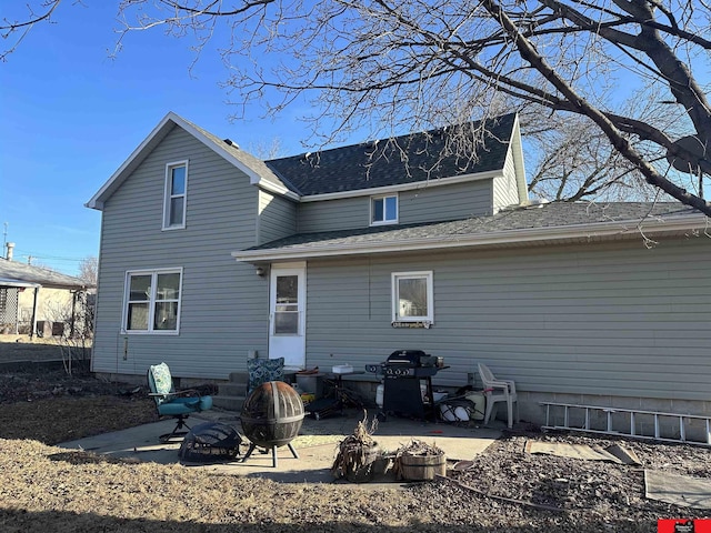 rear view of property featuring a patio area, roof with shingles, and an outdoor fire pit