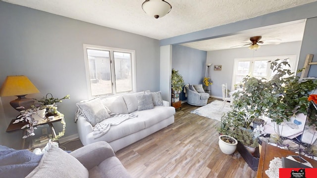 living area featuring ceiling fan, a textured ceiling, baseboards, and wood finished floors