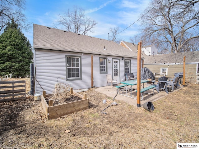 rear view of house with fence, a vegetable garden, a shingled roof, and a patio area