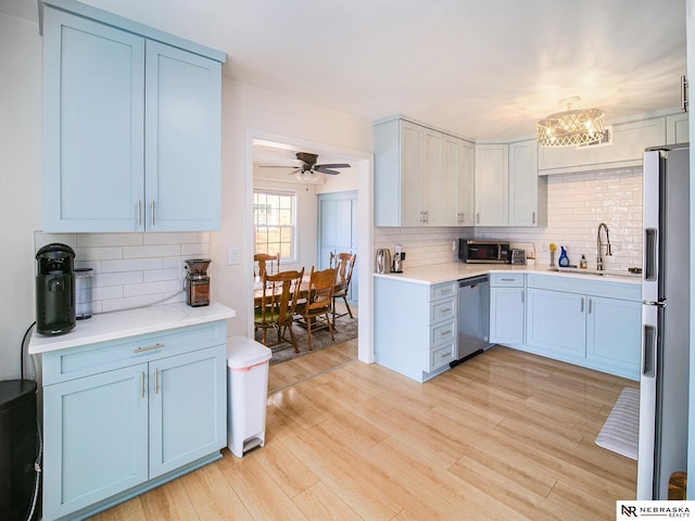 kitchen with light wood finished floors, a sink, tasteful backsplash, stainless steel appliances, and light countertops