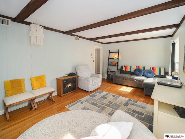 living area featuring visible vents, beam ceiling, and wood finished floors