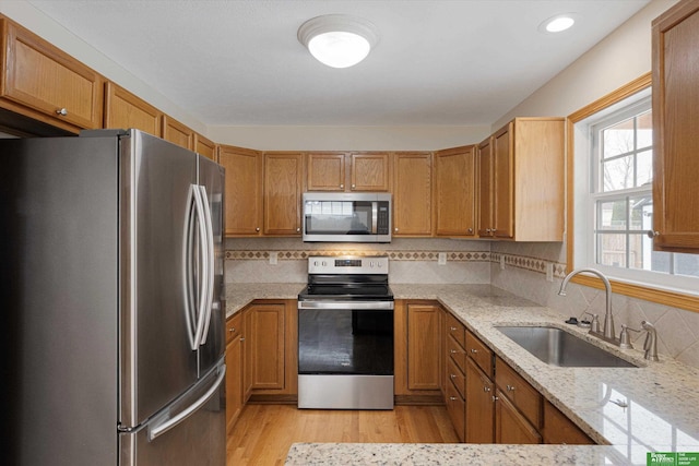 kitchen with light wood-style flooring, a sink, tasteful backsplash, appliances with stainless steel finishes, and light stone countertops