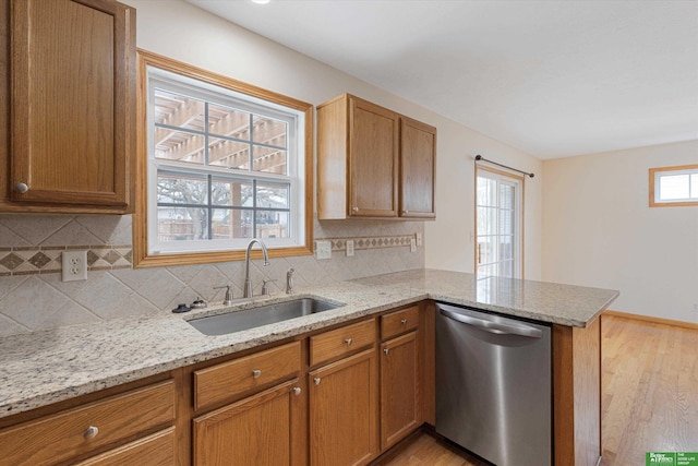 kitchen featuring stainless steel dishwasher, a peninsula, light wood-type flooring, and a sink