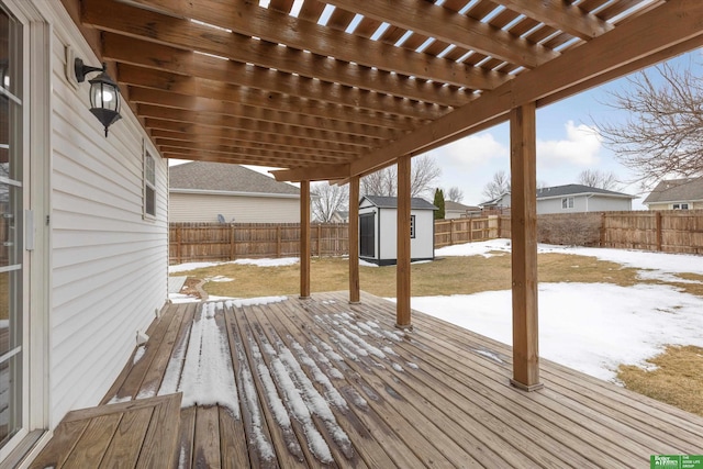 snow covered deck with a pergola, a lawn, a fenced backyard, an outbuilding, and a storage unit