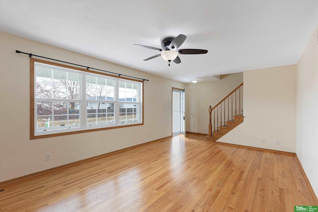 unfurnished room with stairway, light wood-style flooring, a ceiling fan, and baseboards