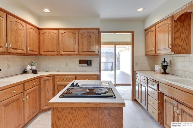 kitchen featuring black electric cooktop, backsplash, a center island, and light countertops