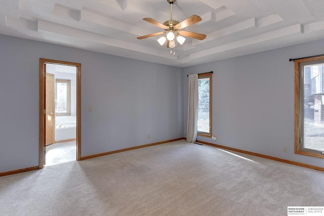 unfurnished room with visible vents, a tray ceiling, baseboards, light colored carpet, and ceiling fan