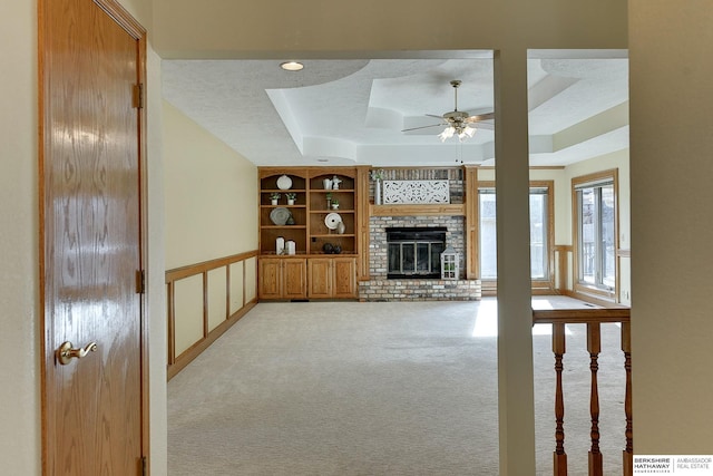 unfurnished living room featuring a textured ceiling, built in features, a fireplace, light carpet, and a raised ceiling