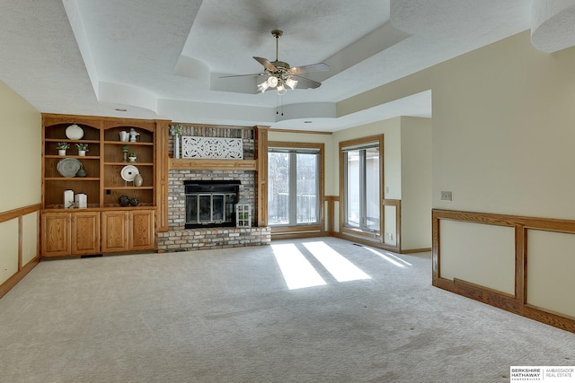 unfurnished living room with a textured ceiling, baseboards, a tray ceiling, light carpet, and a brick fireplace