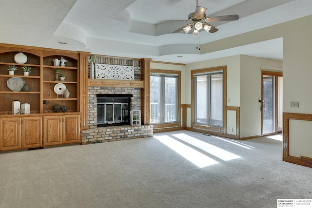 unfurnished living room with a wainscoted wall, light colored carpet, a fireplace, and a raised ceiling