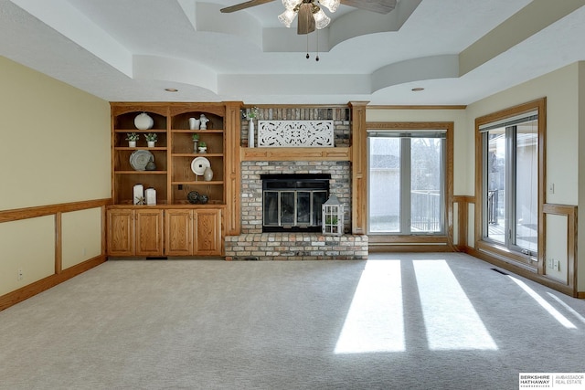 unfurnished living room with visible vents, a brick fireplace, ceiling fan, a tray ceiling, and light carpet