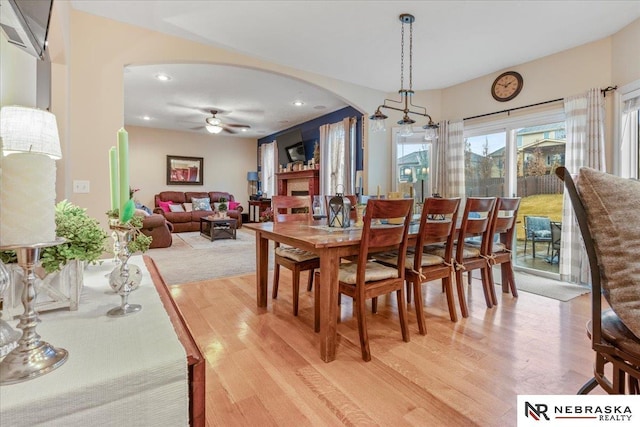 dining area featuring light wood-type flooring, a ceiling fan, recessed lighting, arched walkways, and a fireplace