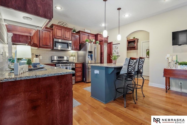 kitchen with light wood finished floors, a breakfast bar area, appliances with stainless steel finishes, arched walkways, and hanging light fixtures