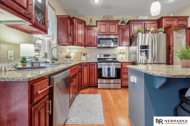 kitchen with dark brown cabinets, light stone countertops, light wood-style flooring, stainless steel appliances, and a sink