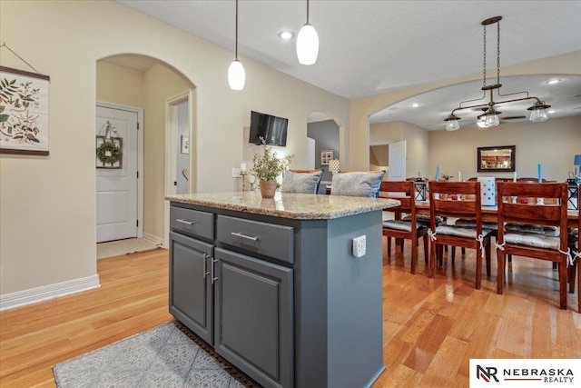 kitchen featuring gray cabinetry, a center island, light wood-type flooring, hanging light fixtures, and arched walkways