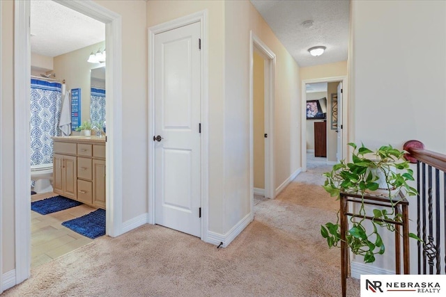 corridor featuring light colored carpet, a textured ceiling, and baseboards