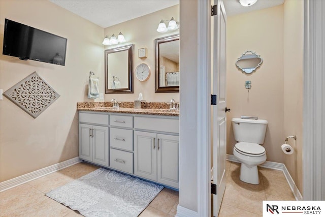 bathroom with tile patterned floors, toilet, a sink, double vanity, and baseboards