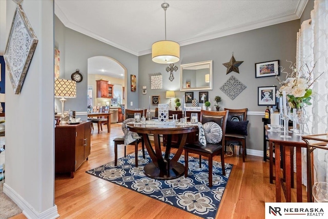 dining room with arched walkways, light wood finished floors, baseboards, and ornamental molding