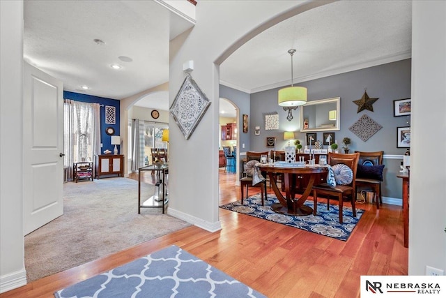 dining area featuring baseboards, arched walkways, wood finished floors, and ornamental molding