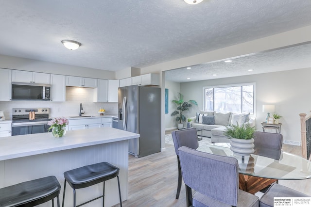 kitchen with a sink, stainless steel appliances, light countertops, white cabinets, and a kitchen breakfast bar