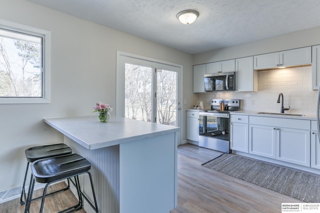 kitchen featuring a sink, a kitchen breakfast bar, stainless steel appliances, light wood-style floors, and decorative backsplash