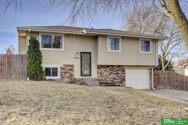 split foyer home featuring brick siding, an attached garage, a front lawn, and fence