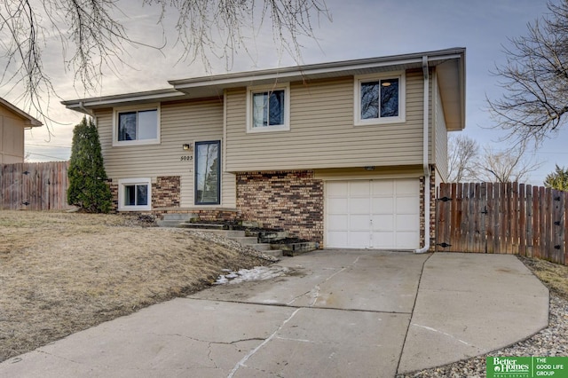 split foyer home featuring driveway, brick siding, an attached garage, and fence