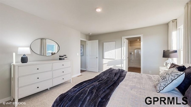 bedroom featuring ensuite bath, light colored carpet, and baseboards