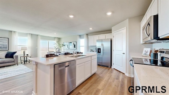 kitchen with a sink, stainless steel appliances, open floor plan, white cabinetry, and light wood-type flooring