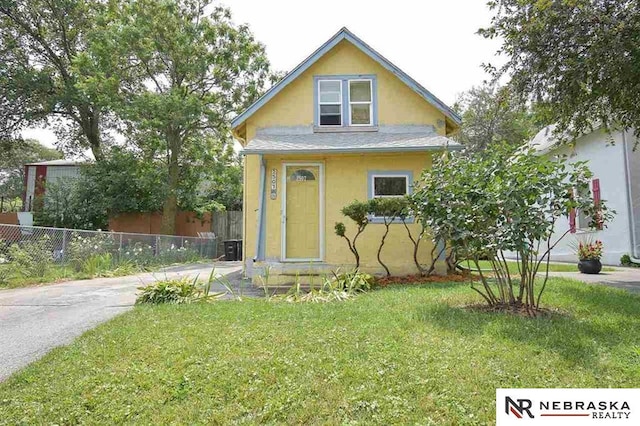 bungalow-style home with stucco siding, roof with shingles, a front yard, and fence