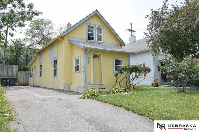 view of front of house with a front yard, fence, a shingled roof, a chimney, and stucco siding