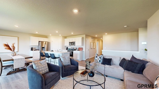 living area featuring recessed lighting, visible vents, light wood finished floors, and a textured ceiling