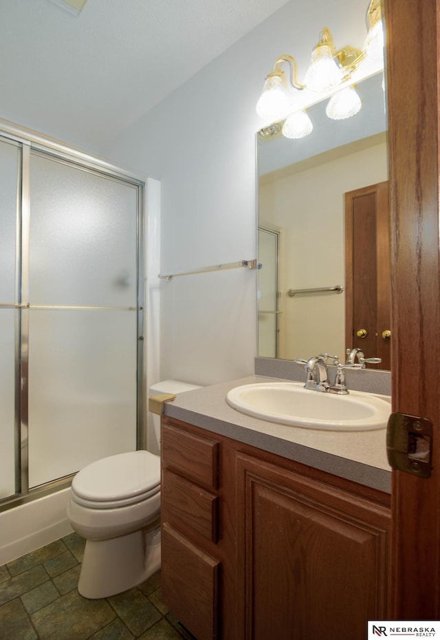 full bathroom featuring a shower with door, stone finish flooring, toilet, and vanity