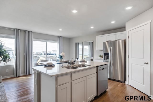 kitchen featuring a center island with sink, a sink, wood finished floors, white cabinetry, and appliances with stainless steel finishes