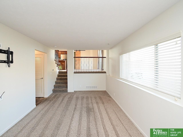 spare room featuring visible vents, baseboards, stairway, light carpet, and a textured ceiling