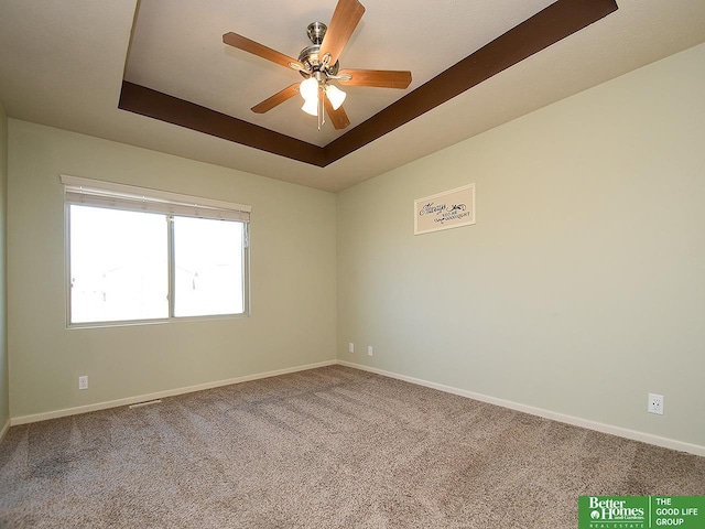 carpeted empty room with a tray ceiling, baseboards, and a ceiling fan