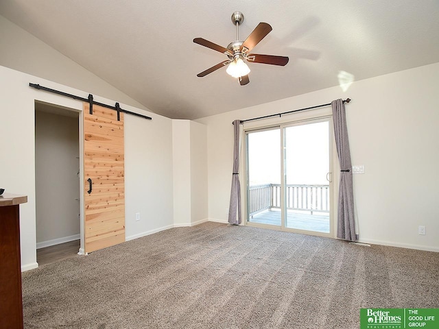 carpeted spare room with ceiling fan, a barn door, baseboards, and vaulted ceiling