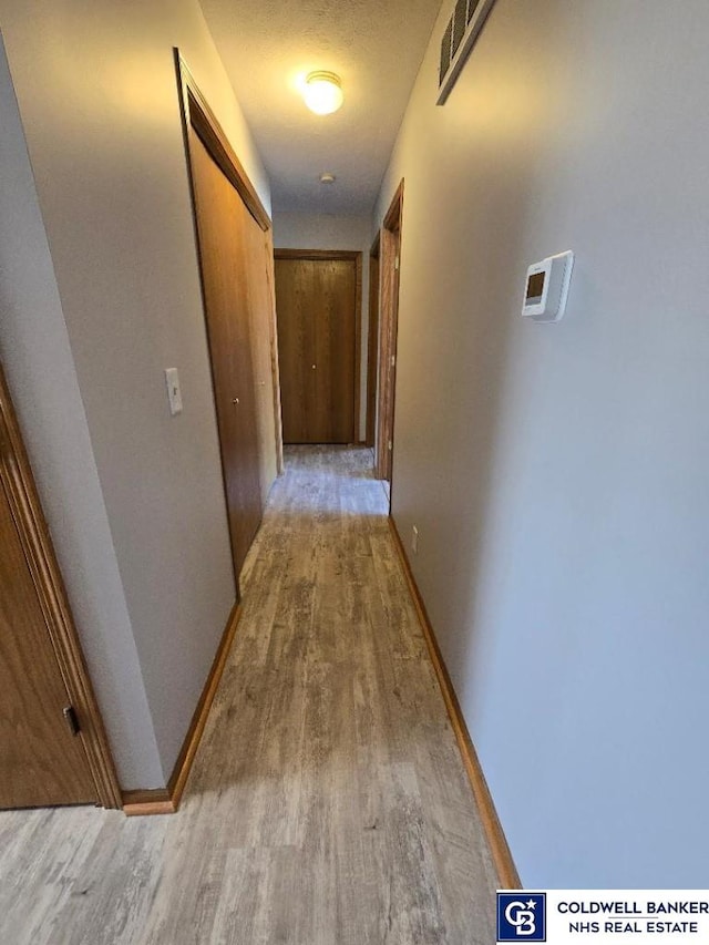 hallway with wood finished floors, visible vents, and baseboards